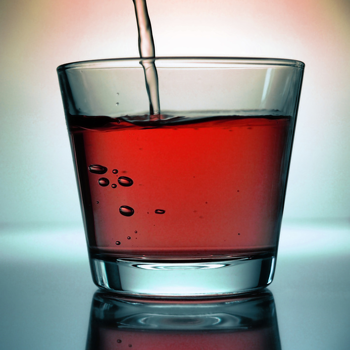 Ein Glas mit roter Flüssigkeit wird mit weiterer Flüssigkeit gefüllt. Saftschorle