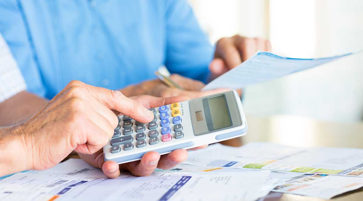 Hände zweier älterer Personen mit Unterlagen und einem Taschenrechner