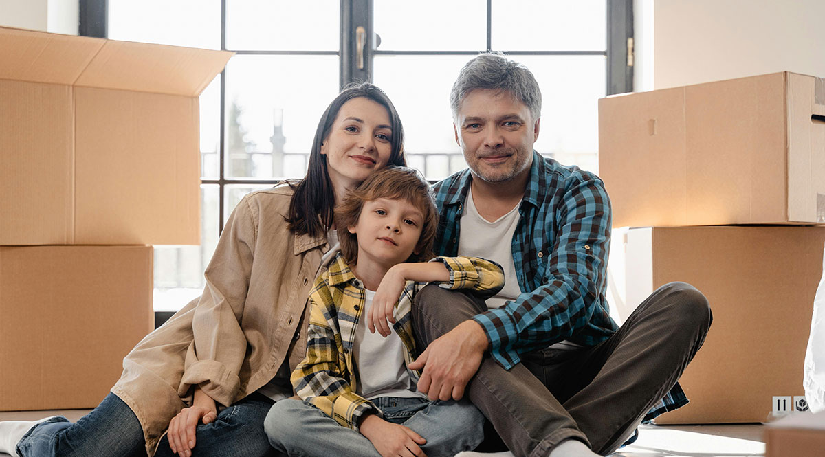 Ein Paar mit Kind sitz vor Umzugskisten in einer leeren Wohnung