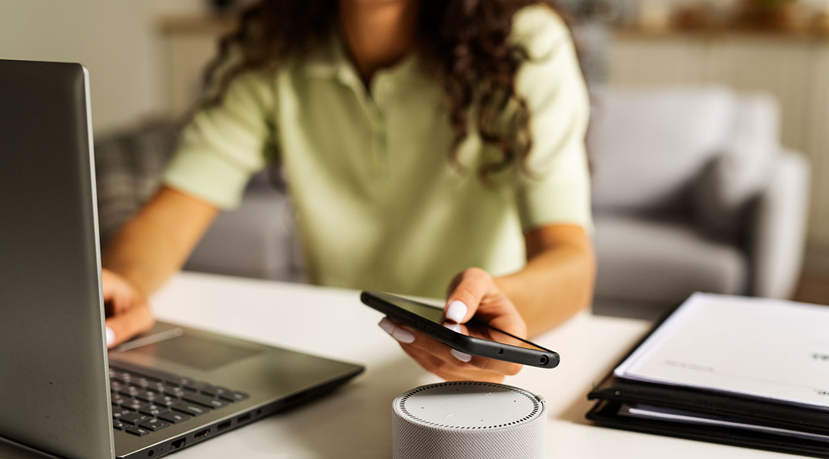 Eine Frau sitzt am Schreibtisch vor einem Laptop, ein Smartphone in der Hand