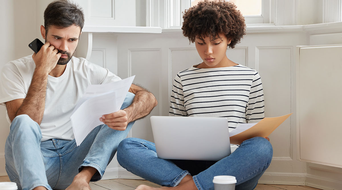Ein Paar sitzt mit Telefon und Laptop in einer Wohnung auf dem Boden