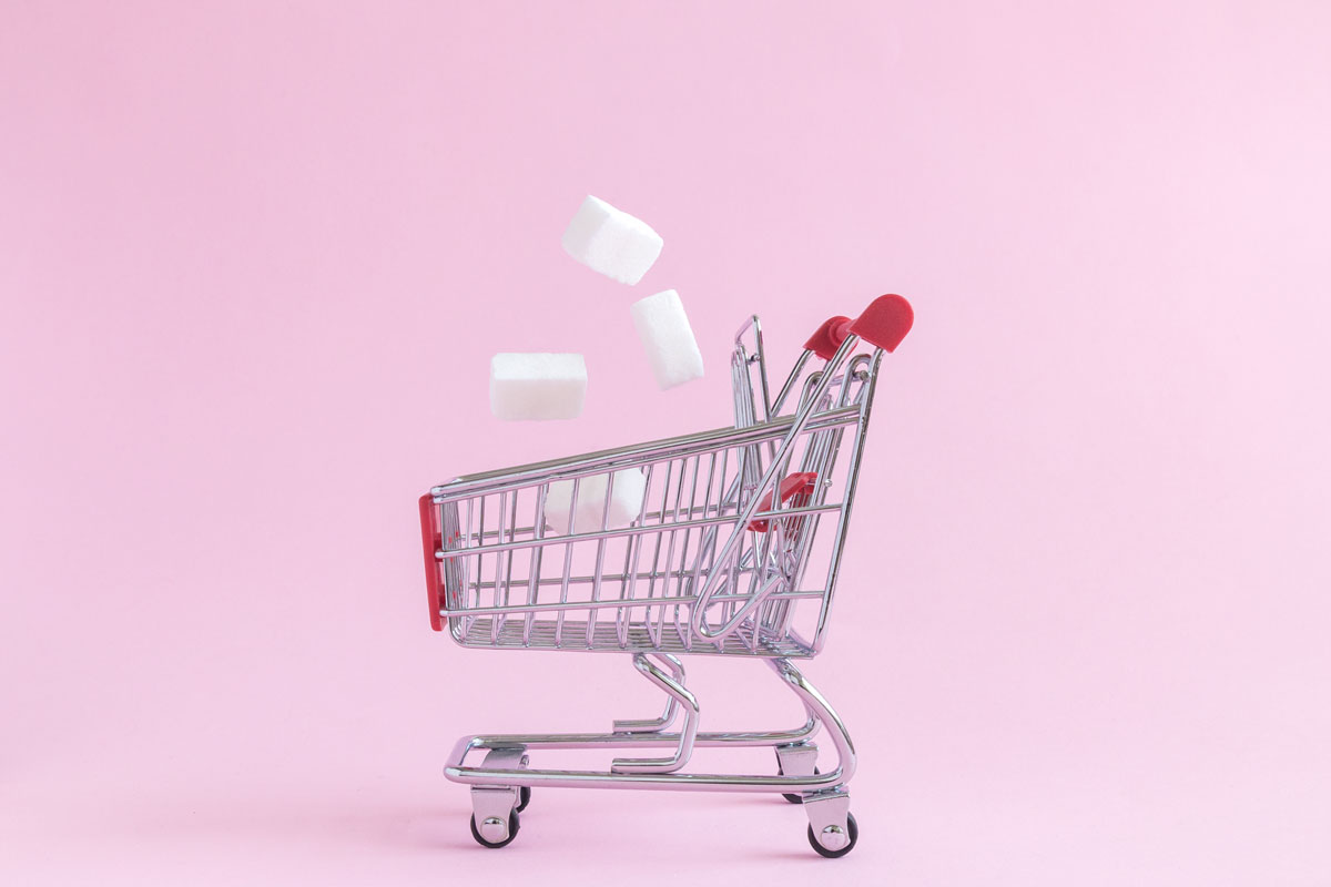 Einkaufswagen vor rosa Hintergrund, Zuckerwürfel fallen hinein