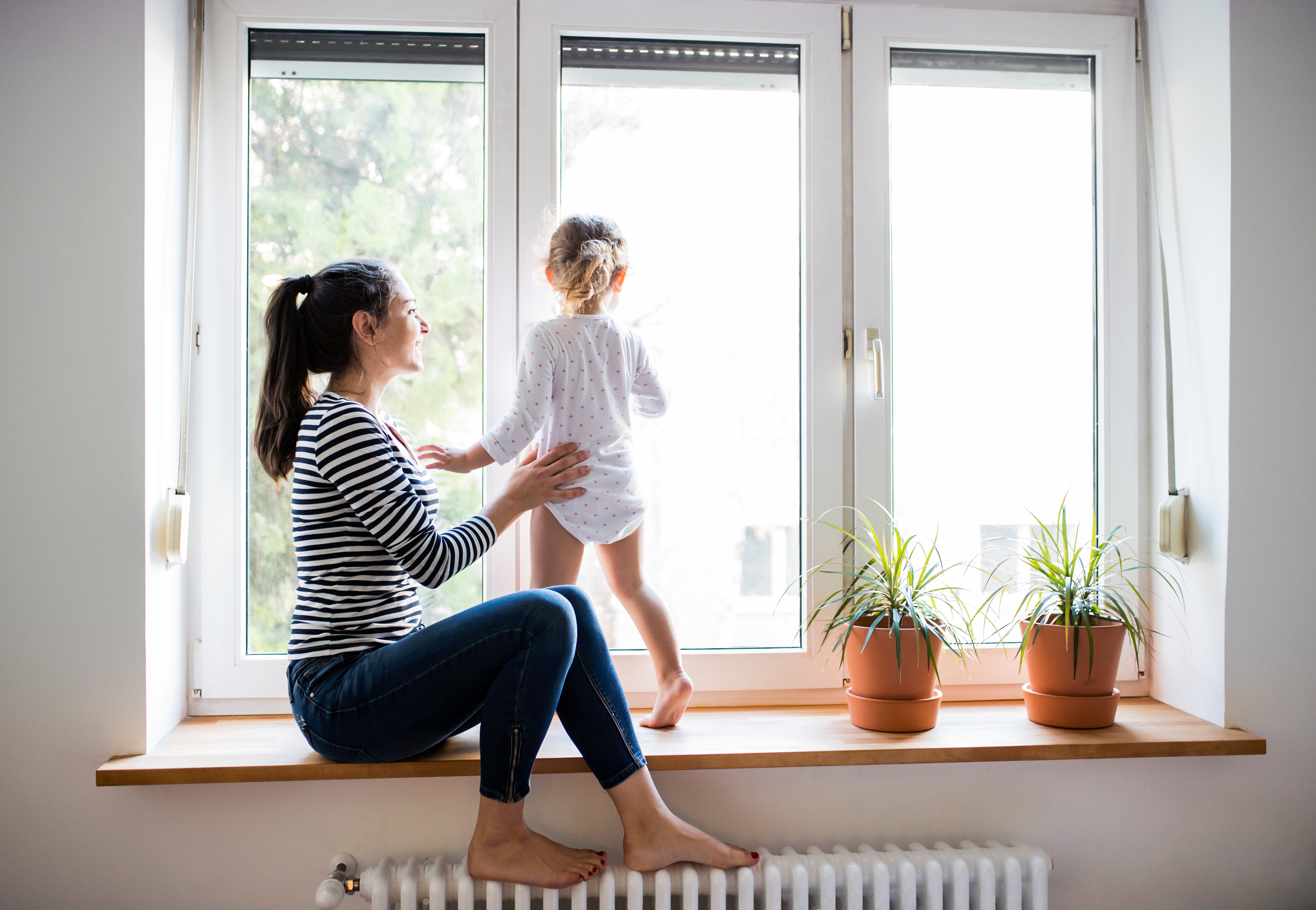 Eine Frau sitzt auf einer Fensterbank, ein Kind steht daneben und sieht aus dem Fenster