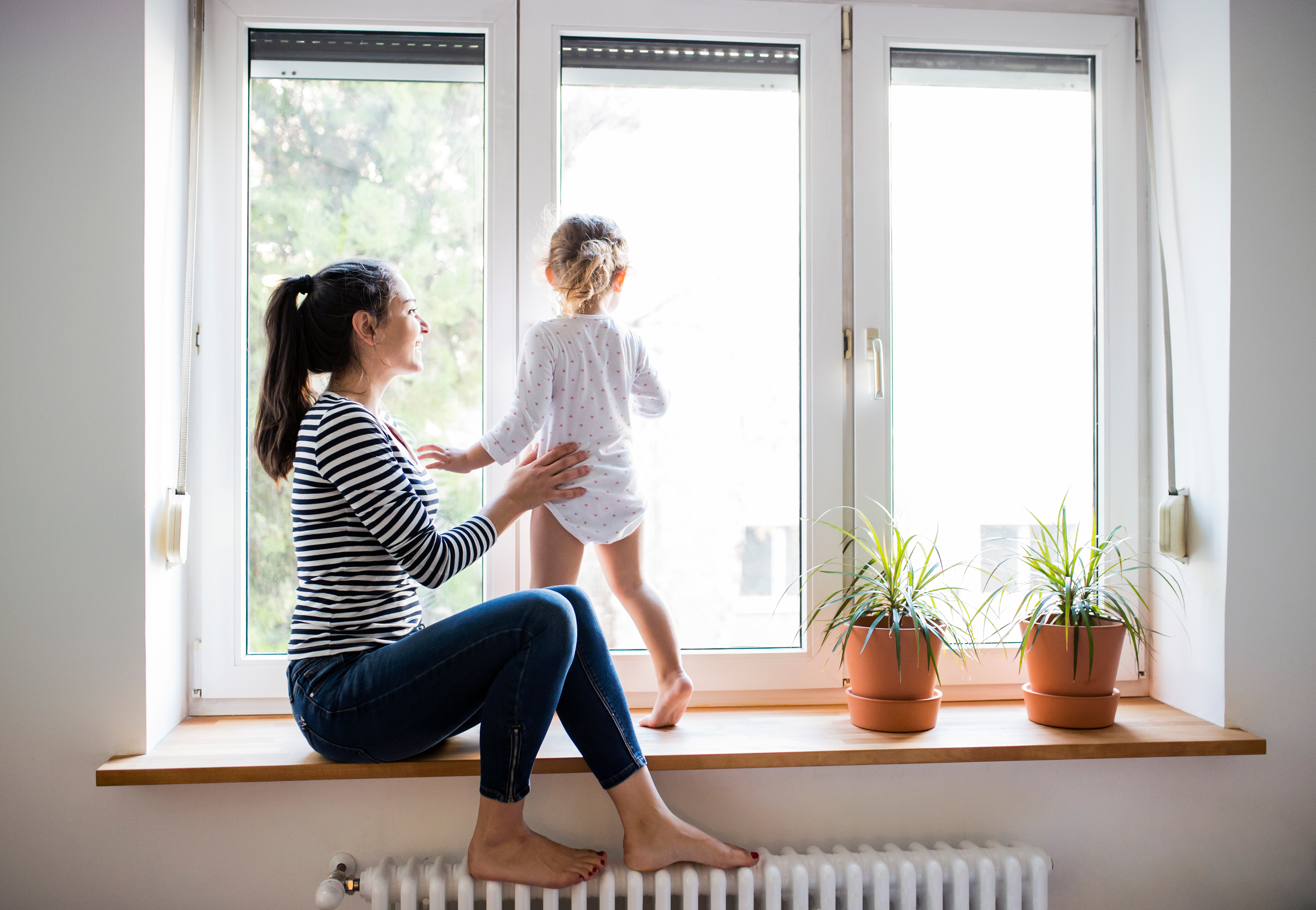 Eine Frau sitzt auf einer Fensterbank, ein Kind steht daneben und sieht aus dem Fenster