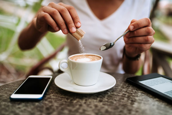 Jung Frau schüttet Zucker in eine Tasse Cappuccino