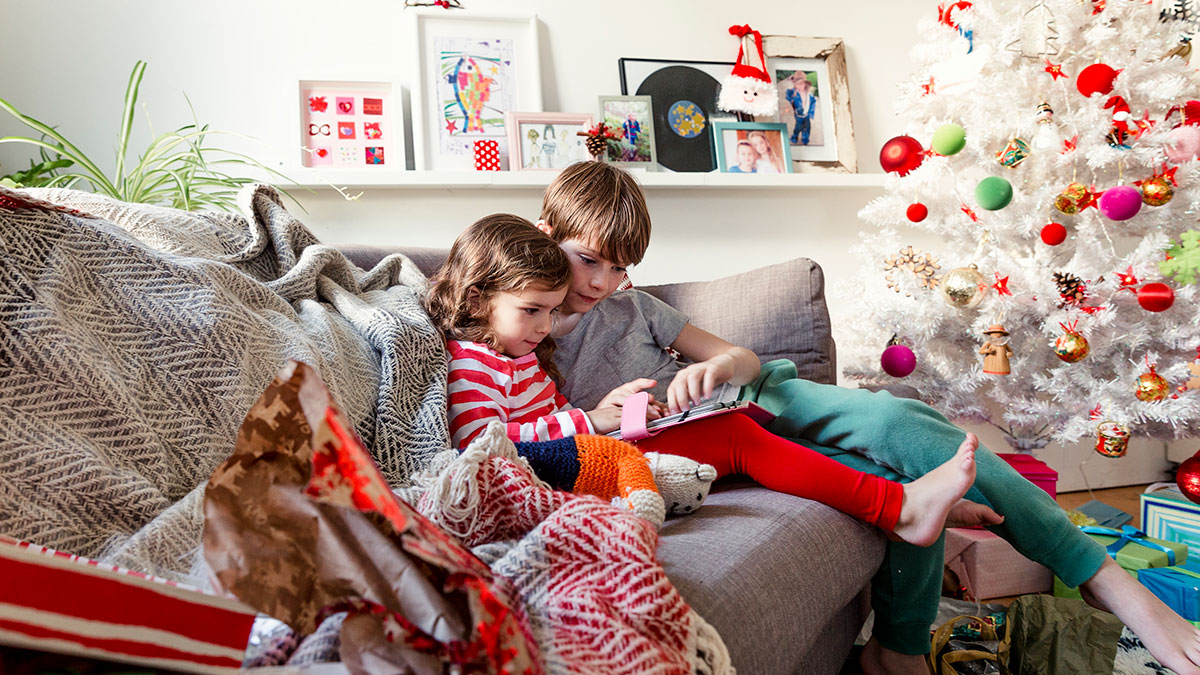 Mädchen und Junge sitzen auf einem Sofa im weihnachtlich geschmückten Zimmer