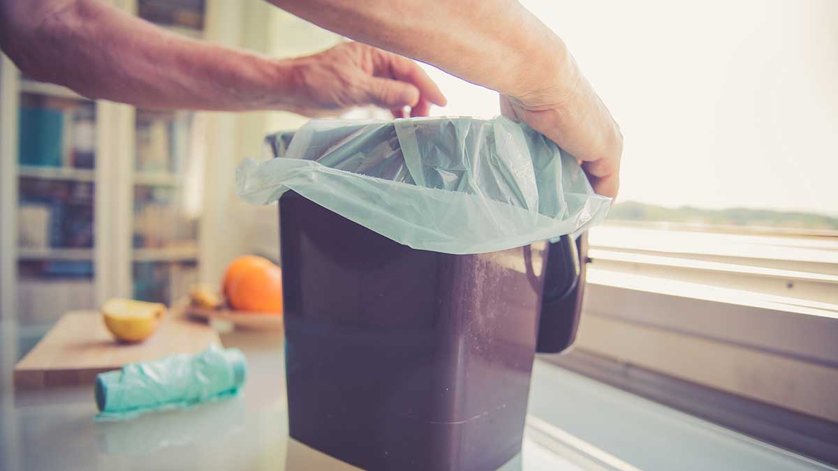 Plastik-Alternativen: Männerhände legen eine Bio-Mülltüte in einen Mülleimer ein