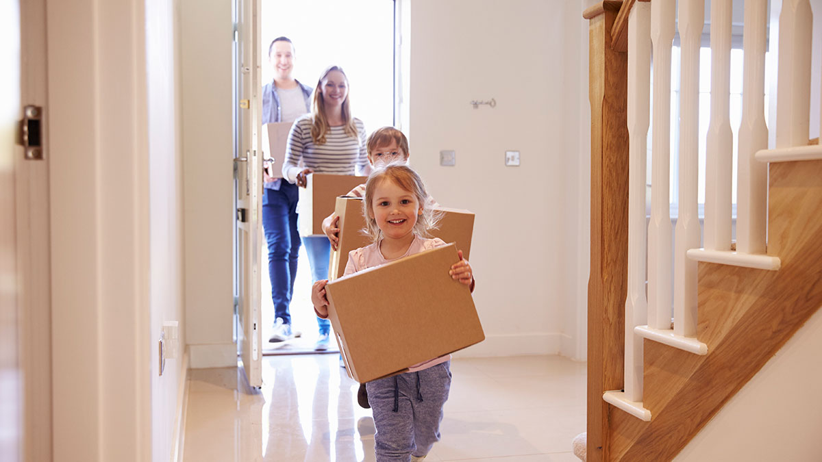 Eine Familien läuft mit Umzugskisten in ihr neues Haus