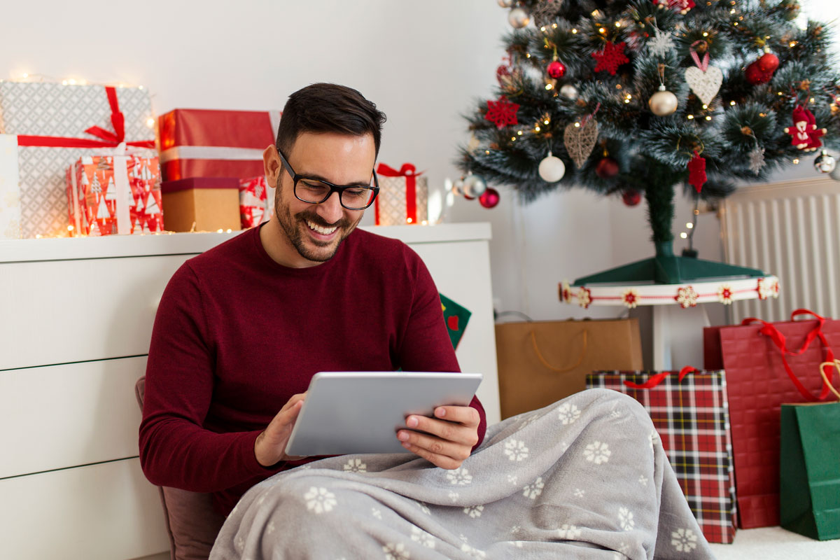 Junger Mann mit Laptop im weihnachtlich geschmückten Zimmer