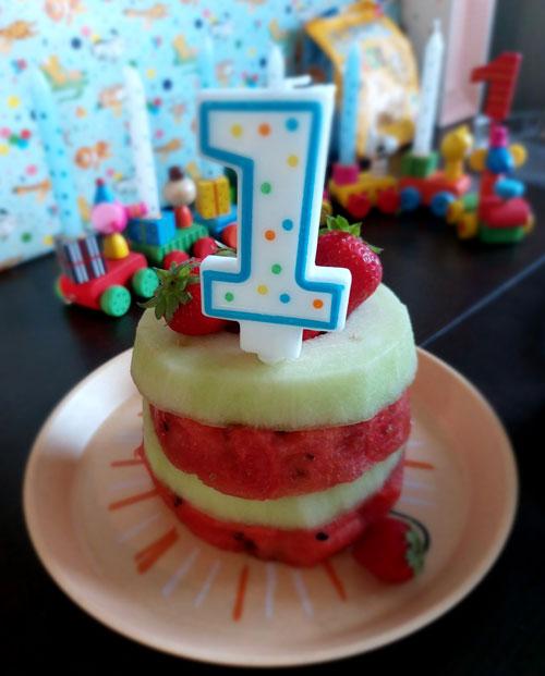 Eine kleine Schichttorte, die aus verschiedenen Melonenscheiben zusammengesetzt und mit Erdbeeren dekoriert ist, mit einer Geburtstagskerze