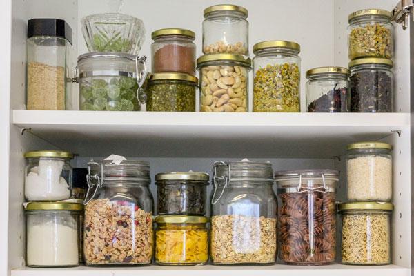 Ein Schrank mit mehreren Vorratsgläsern, darin  Müsli, Nüsse, Nudeln und andere trockene Vorräte 