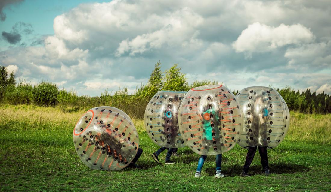 Jugendliche spielen auf einer Wiese in großen aufblasbaren Gummibällen (Bumperballs)  