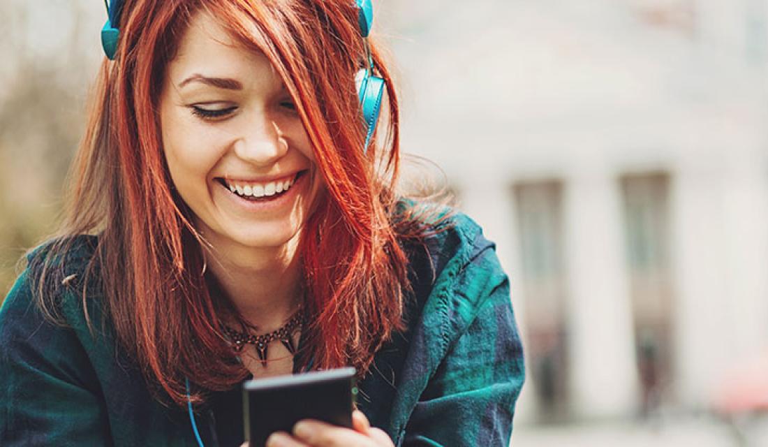 Verbraucherschutz spielend lernen: Eine lachende junge Frau mit Smartphone und Kopfhörern