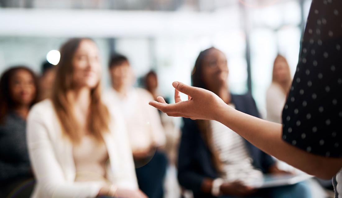 Jemand erklärt etwas, im Hintergrund schemenhaft sitzendes Publikum