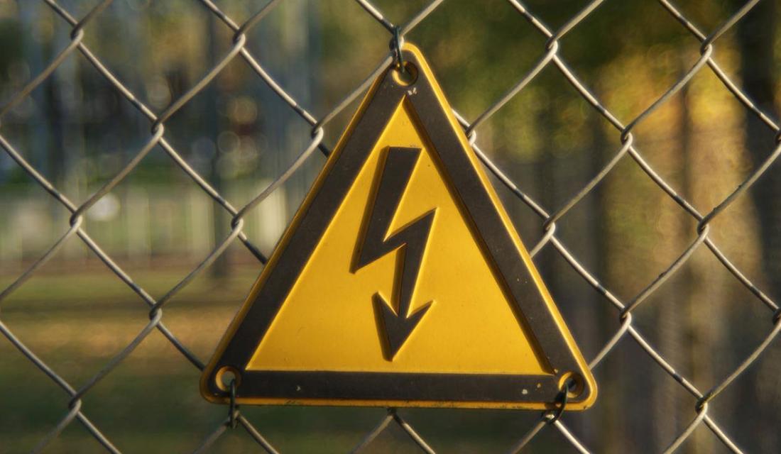 An einem Zahn hängt ein gelbes dreieckiges Warnschild, das vor Hochspannung/Elektrizität warnt