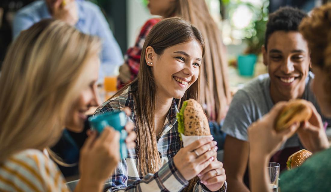 Eine Gruppe Jugendlicher isst und trinkt an einem Tisch in einer Mensa
