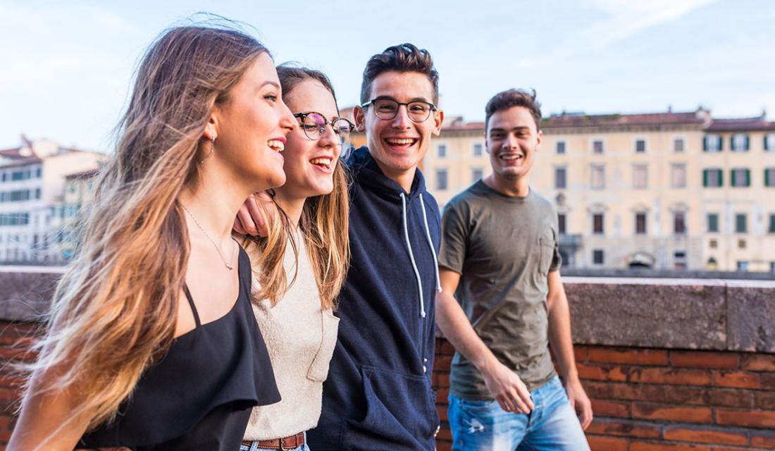 Vier fröhliche Jugendliche laufen eingehakt nebeneinander