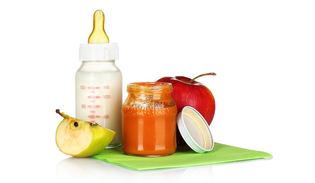 Ein Babyfläschchen mit Milch, Apfelschnitze und ein Glas Gemüsebrei