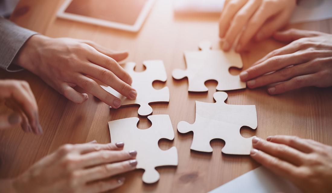 Mehrere Händepaare legen auf einem Tisch vier große Holz-Puzzleteile zusammen