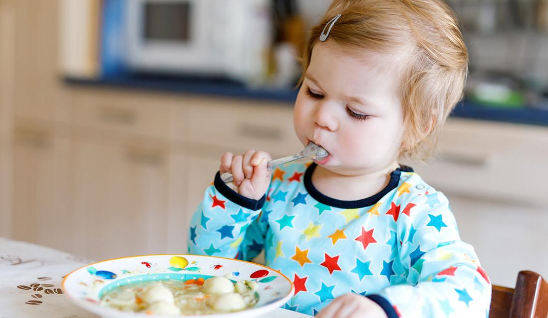 Ein Kleinkind sitzt am Tisch vor einem Teller Suppe 