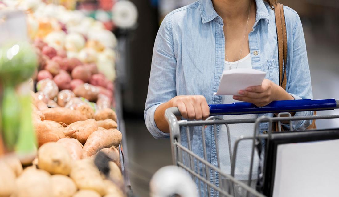 Eine Frau schiebt den Einkaufswagen an einer Regalfläche mit Gemüse vorbei