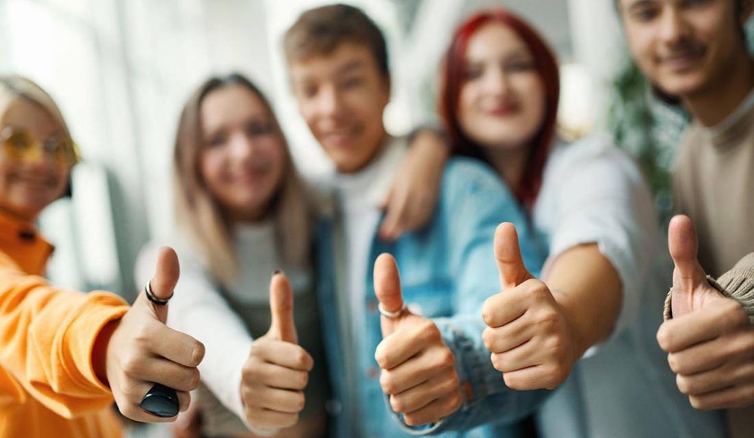 Vier jugendliche  unscharf in Hintergrund, die das "Daumen-hoch"-Symbol machen