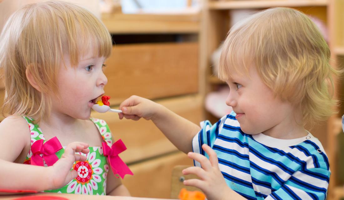 Ein Kind füttert ein anderes mit einem Löffel