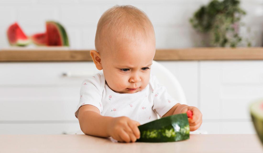 Ein Kleinkind betrachtet und befühlt ein Stück Wassermelone