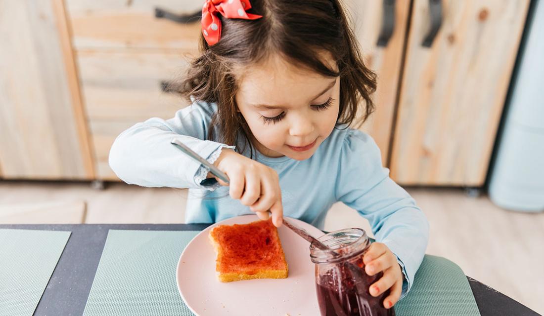 Ein Mädchen bereitet sich ein Brot mit Marmelade zu