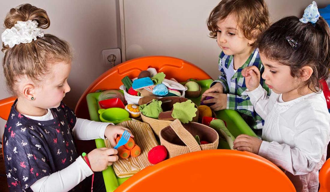 Kita-Kinder sitzen an einem Tisch und bereiten mit Spielzeug-Gemüse essen zu