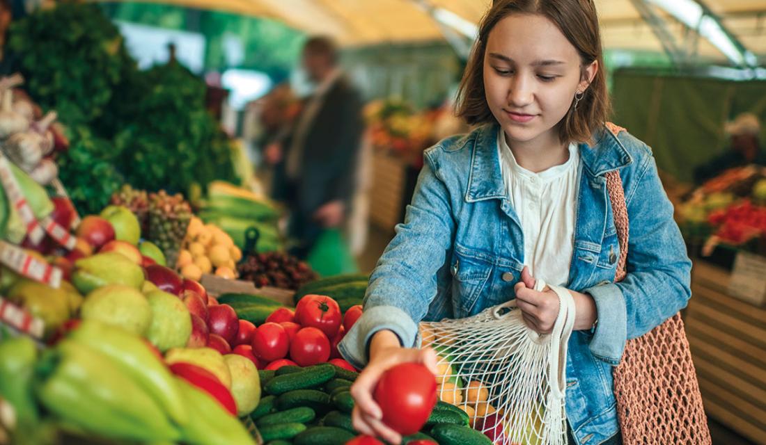 Eine junge Frau kauft unverpacktes Gemüse an einem Stand ein.