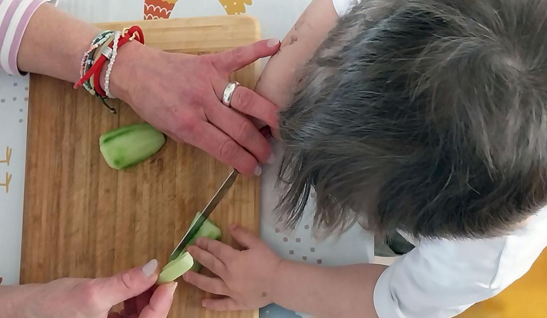 Blicke aus der Vogelperspektive: Hände unterstützen ein Kind beim Schneiden einer Gurke 