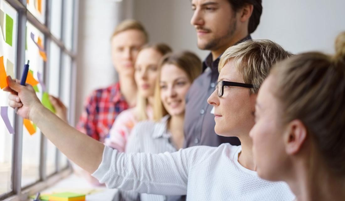 eine Gruppe Menschen klebt PostIts an eine Pinnwand