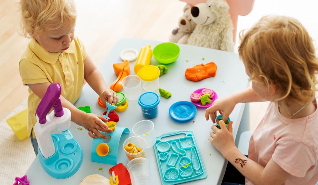 Zwei Kleinkinder basteln am Tisch mit farbiger Knete