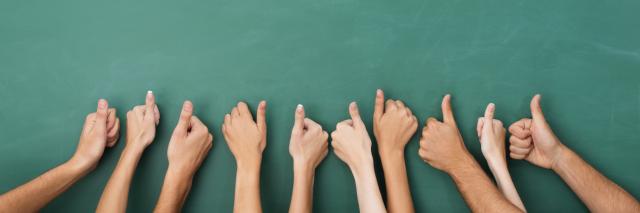 Viele Arme mit hochgereckten Daumen vor einer grünen Schultafel