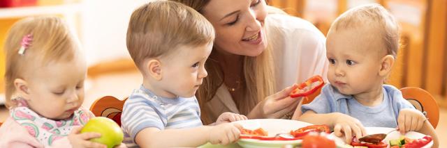Eine Frau sitzt mit drei Kleinkindern beim Essen am Tisch
