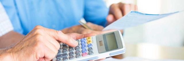 Hände zweier älterer Personen mit Unterlagen und einem Taschenrechner