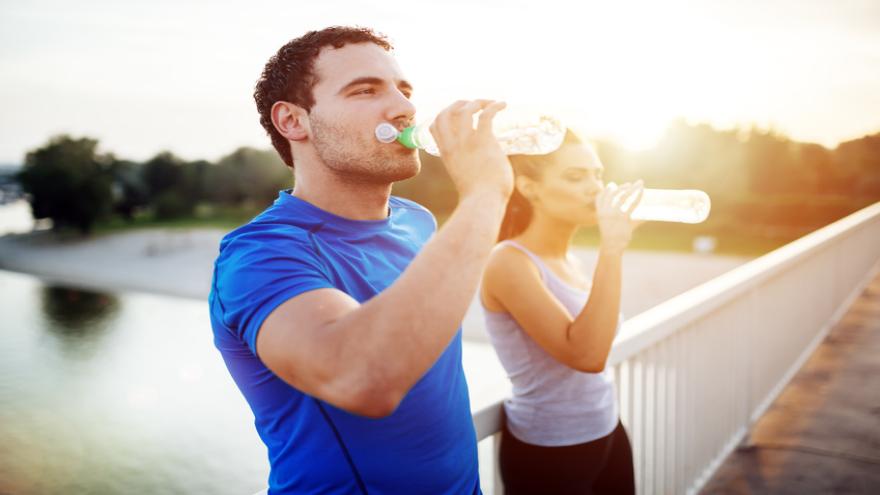 Sportler und Sportlerin trinken aus Flaschen, sie stehen auf einer Brücke im Abendlicht