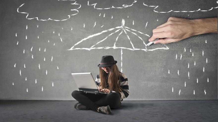 Junge Frau sitzt mit Laptop auf dem Boden, eine große Hand zeichnet mit Kreide eine Regenschirm über ihren Kopif