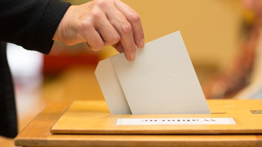 Jemand wirft einen Stimmzettel in eine Wahlurne