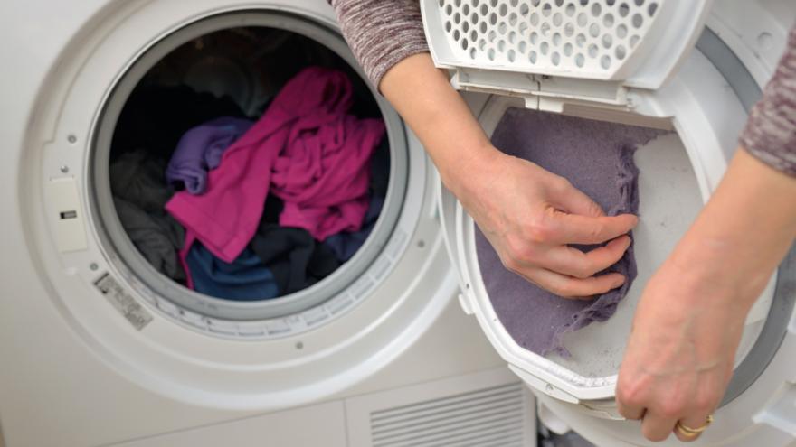 Eine Frau reinigt das Flusensieb eines Wäschetrockners