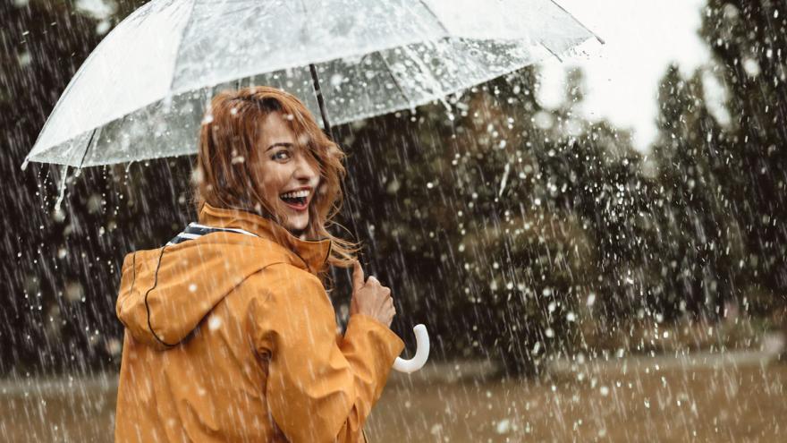 Junge Frau geht im Regen unter einem Regenschirm spazieren