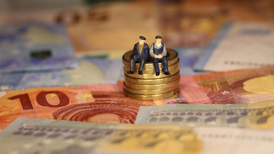 Miniaturfiguren von Senioren sitzen auf einem kleinen Stapel Geldmünzen und Scheine