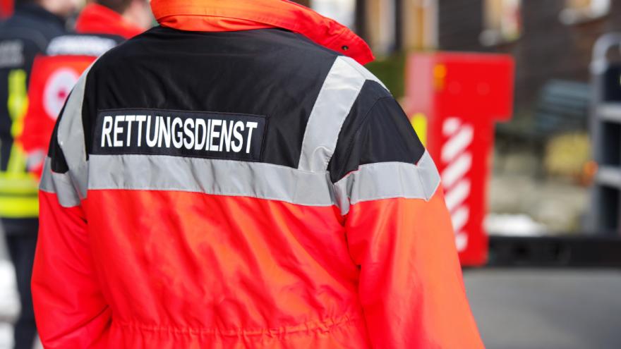 Jemand steht an einer Straße und trägt eine Warnweste, auf der "Rettungsdienst" steht.