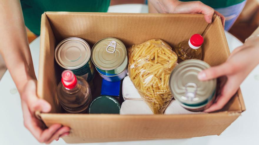 Mehr Müll aus Verpackung durch Corona: Hände halten ein Paket mit Konservendosen und verpackten Nudeln 