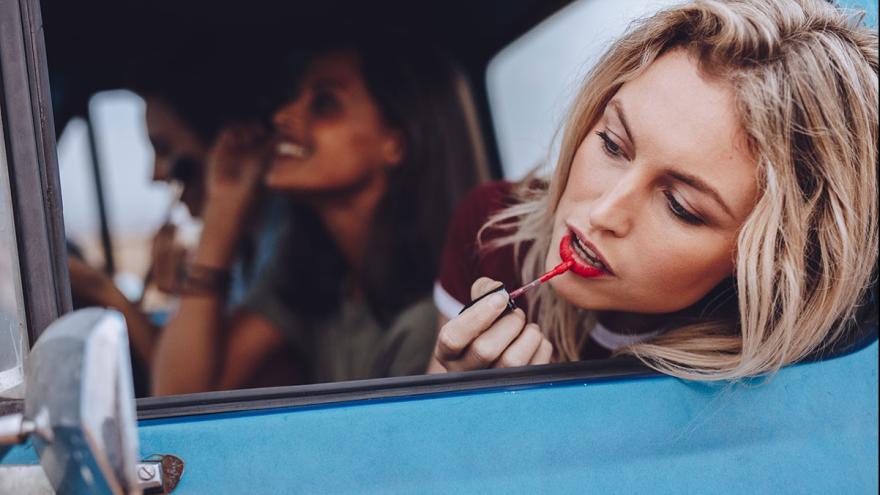 Zwei Frauen in einem blauen Auto, eine malt sich die Lippen an