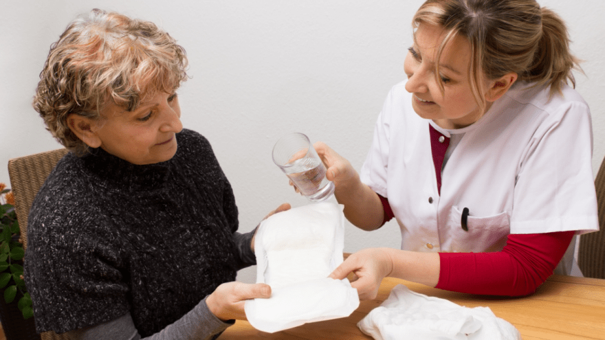 Eine Frau erklärt einer anderen eine Inkontinenzhilfe, die sie in der Hand hält.