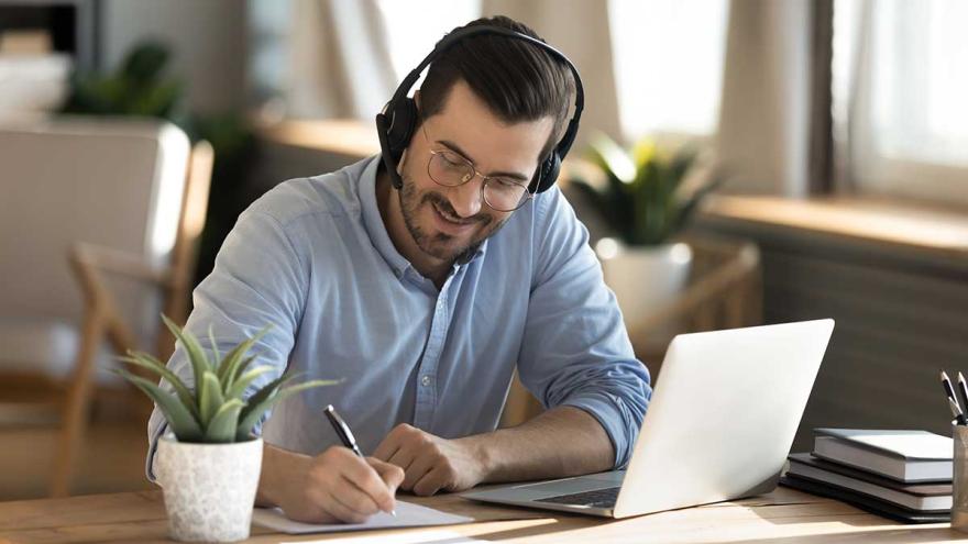 Videoberatung: Ein Mann sitzt mit Laptop und Headset an einem Tisch und macht Notizen