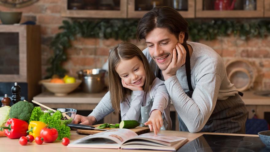 Abwechslungsreiche Familienküche: Ein Mann und ein Mädchen in der Küche betrachten ein Kochbuch 