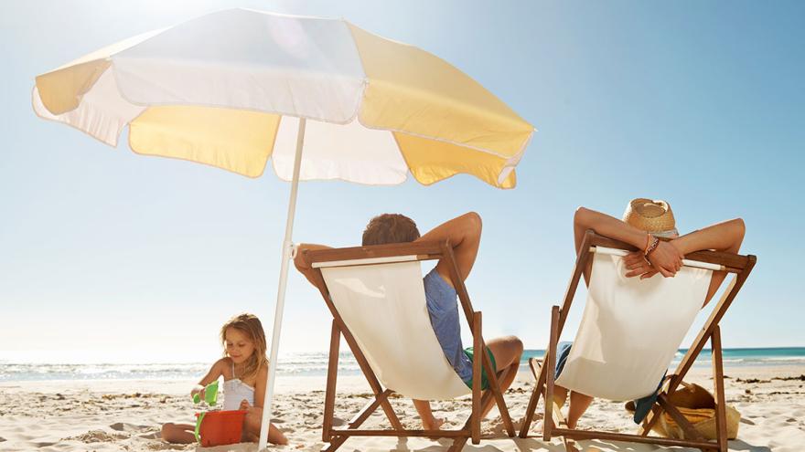 Reiserecht: Ein Paar sitzt am Strand in Liegestühlen, ein Mädchen spielt daneben im Sand 